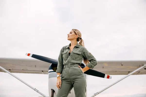 portrait of beautiful blonde pilot woman in front of airplane