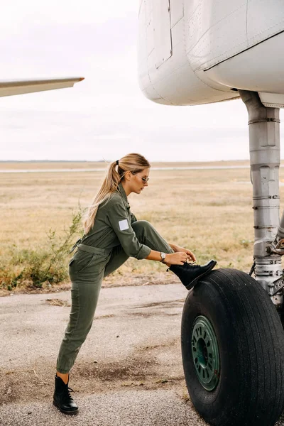 portrait of beautiful blonde pilot woman in front of airplane