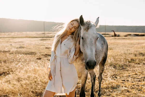 portrait of beautiful blonde woman with white horse on nature during sunset