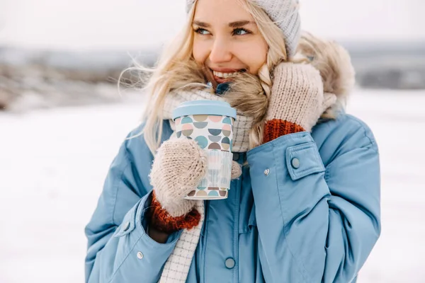 冬の日にコーヒーの再利用可能なカップと陽気な若いブロンドの女性のクローズアップポートレート — ストック写真