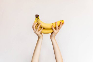 Beyaz arka planda olgun muzları tutan kadın..