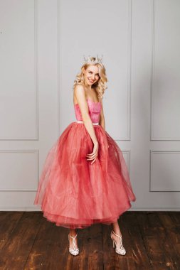 Pembe tül elbise ve taç giyen mutlu genç bir kadın poz veriyor ve gülümsüyor..