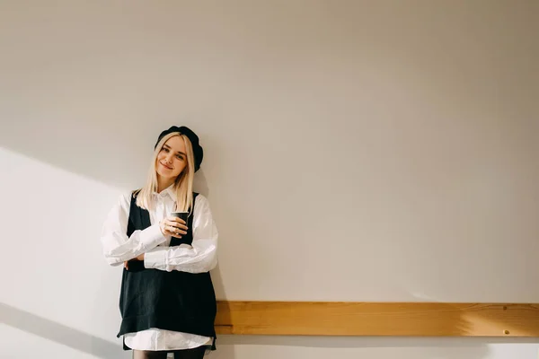年轻快乐的金发女人站在白墙边 举着一杯咖啡 面带微笑 — 图库照片