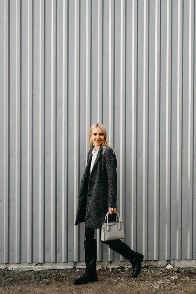 穿着灰色金属墙背景的时髦年轻女子在街上行走 — 图库照片