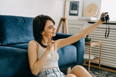 Genç esmer kadın evde klasik bir kamerayla kendi portresini çekiyor, gülümsüyor..