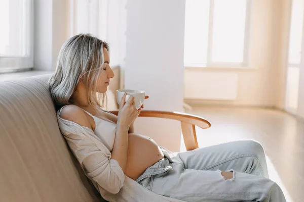 妊娠中の女性はコーヒーや紅茶を飲みながら家でソファに座って ストック画像