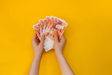 Sarı arka planda bir avuç sterlin banknotunu tutan bir kadın..