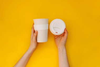 Sarı arka planda yeniden kullanılabilir bambu kahve fincanı tutan kadın eller..