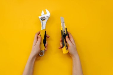 İngiliz anahtarı tutan kadın eller ve sarı arka planda bir kesici..