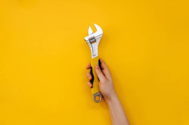 Sarı arka planda İngiliz anahtarı tutan bir kadın..