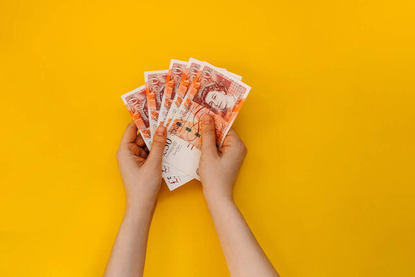 Женщины держат в руках кучу банкнот фунта стерлингов на желтом фоне.