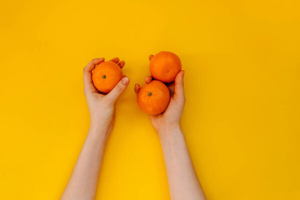 Female hands holding three oranges on yellow background.