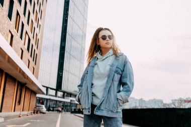 Kot pantolon giyen ve şehir sokaklarında güneş gözlüğü takan genç bir kadın..