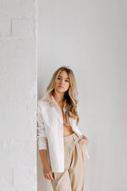 Uzun dalgalı saçlı, rahat beyaz bir gömlek giyen, beyaz arka planda, sarışın bir kadının sakin portresi..