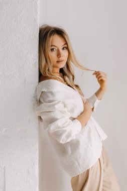 Saçlarıyla oynayan sarışın bir kadının sakin portresi, beyaz gömlekli, kapalı, beyaz arka planda..