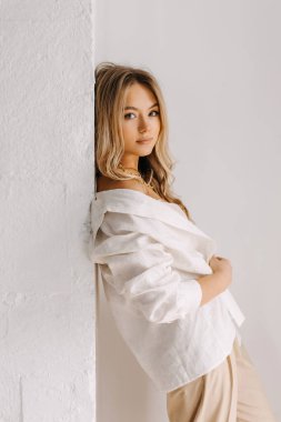 Uzun dalgalı saçlı genç bir kadının portresi. Beyaz arka planda, beyaz, rahat beyaz bir gömlek giyiyor..