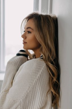 Uzun dalgalı saçlı, süveter kollu genç bir kadının sakin portresi..