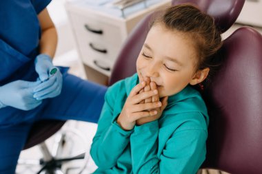 Diş kliniğindeki küçük kız elleriyle ağzını kapatıyor..