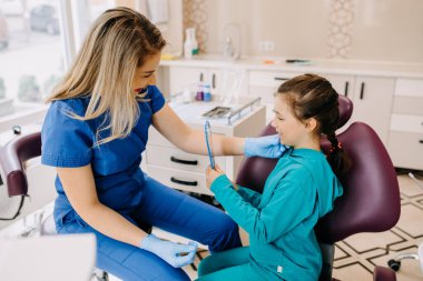 Dişçi hastaya sonuçları aynada gösteriyor. Dişçide çocuk.