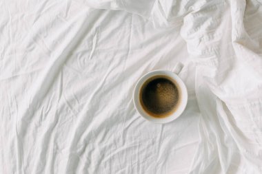 Beyaz çarşafta bir fincan sade kahve. Yatak konseptinde kahvaltı.