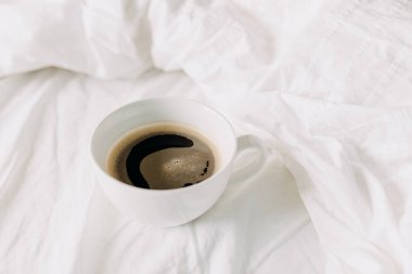 Beyaz çarşafın üzerinde boş beyaz bir fincan kahve. Yatak konseptinde kahvaltı.