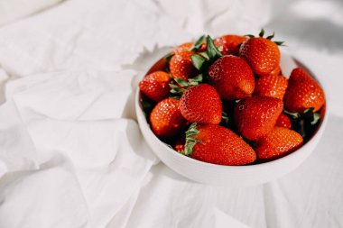 Beyaz bir çarşaf üzerinde organik taze çilek kasesi..