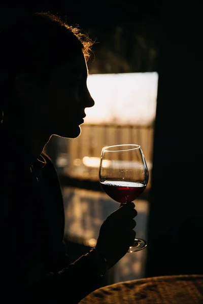 日没の光の中で赤ワインのガラスを持つ若い女性のシルエット — ストック写真