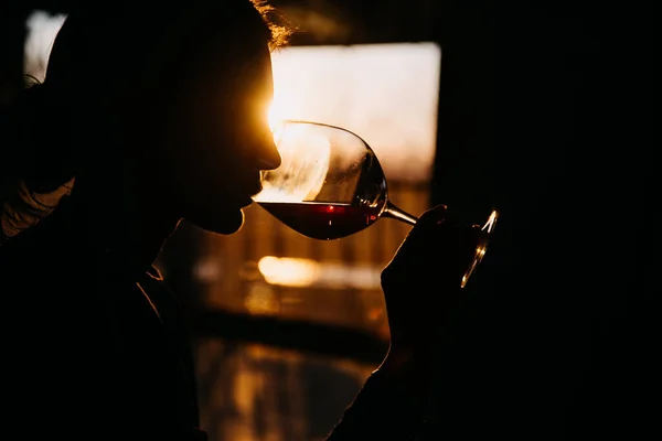 日没の光の中で赤ワインを飲む若い女性のシルエット — ストック写真