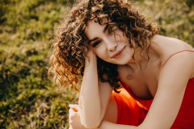 Kıvırcık saçlı, mutlu genç esmer kadın, gülümsüyor, açık havada, bir tarlada, kameraya bakıyor..