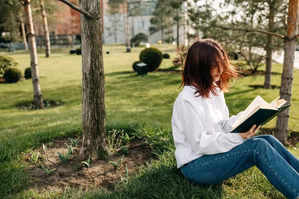 Νεαρή Φοιτήτρια Κάθεται Στο Πράσινο Γρασίδι Ένα Πάρκο Και Διαβάζει — Φωτογραφία Αρχείου