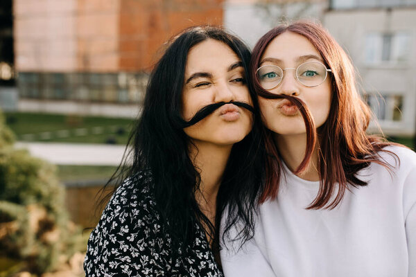 Two best friends making hair mustache, laughing and making funny faces.