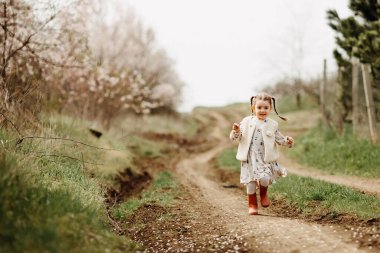 Kauçuk çizmeli, iki örgülü mutlu küçük kız bahar günü kırsalda koşuyor..
