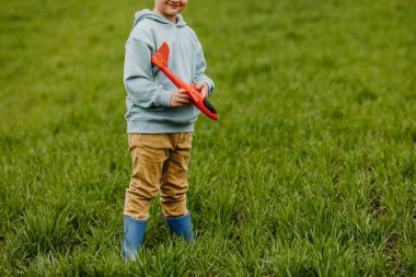 Kırmızı bir uçakla oynayan, yeşil çimlerle kaplı bir arazide duran bir çocuk..