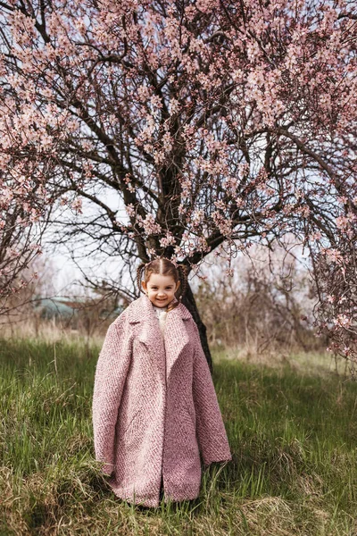 大きな母のコートを着て庭に咲く桜の木の下に — ストック写真