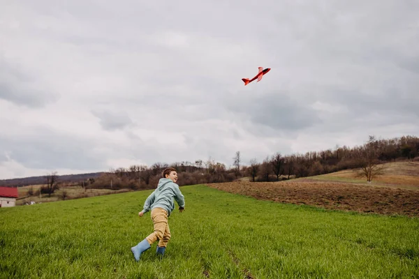 Pojke Kastar Ett Rött Flygplan Spelar Ett Fält Med Grönt — Stockfoto