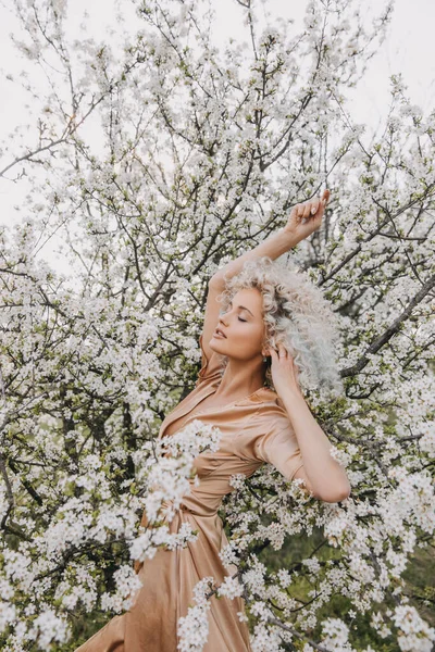 Mladá Blondýnka Kudrnatými Vlasy Hedvábných Šatech Třešňovém Stromě Bílými Květy — Stock fotografie
