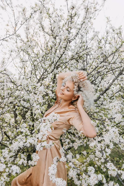 春の日に白い花を持つ桜の木で 中髪の若いブロンドの女性 — ストック写真