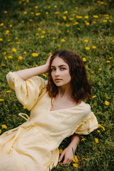 タンポポと緑の芝生のフィールドで黄色のドレスの若い女性 — ストック写真