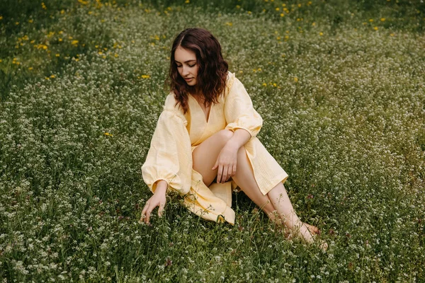 若い裸足の女性は黄色の夏のドレスを着て 緑の芝生のフィールドに座って — ストック写真