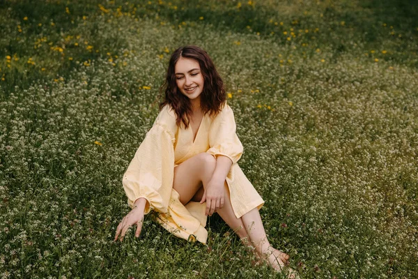 黄色の夏のドレスを着た若い女性は 野の花とフィールドに座って笑顔で — ストック写真