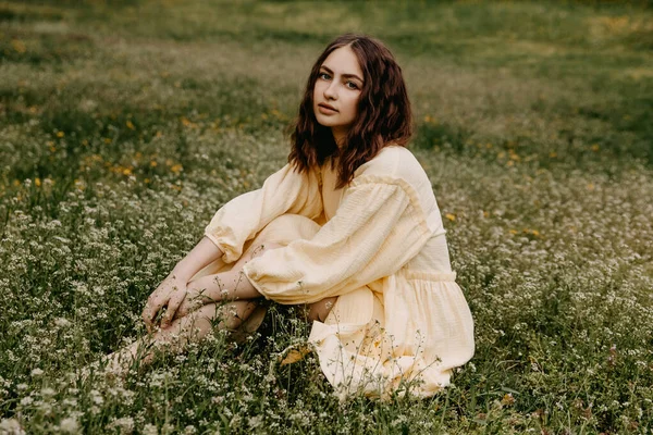 黄色の夏のドレスの若い女性は 緑の芝生のフィールドに座って カメラを見て — ストック写真