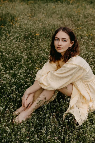 若い裸足の女性は黄色のムスリンのドレスを着て 野の花とフィールドに座って — ストック写真