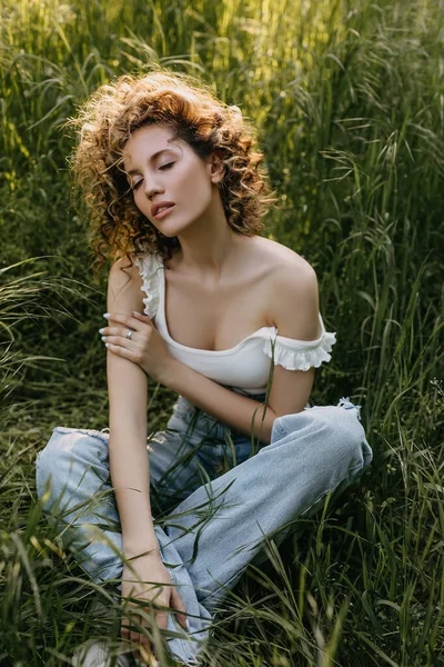背の高い緑の草の牧草地に座って 短い巻き毛を持つ若い女性 — ストック写真