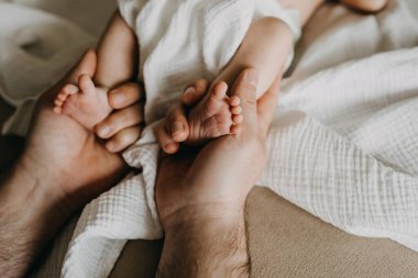 Babanın yeni doğmuş küçük bebek ayaklarını elinde tuttuğu yakın plan..