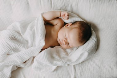 Bebek yuvasında uyuyan yeni doğmuş bir bebek, beyaz çarşafla örtülü..
