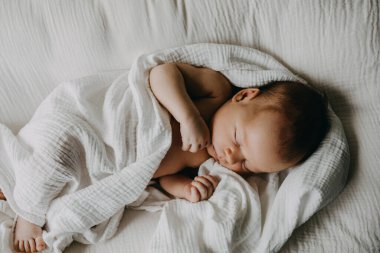 Bebek yuvasında uyuyan yeni doğmuş bir bebek, beyaz çarşafla örtülü..