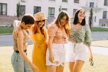 Group of four young women in a park, having good time, hugging and laughing.