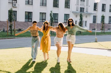 Group of four young women in a park, having good time, hugging and walking.