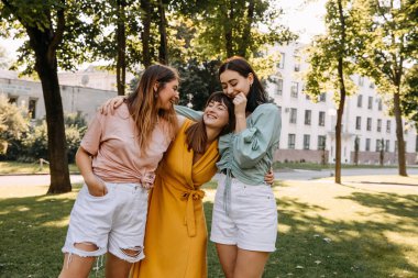 Group of three young women in a park, having good time, hugging and laughing.