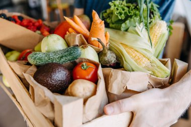 Closeup of man holding a box full of various organic vegetables, fruits and berries.